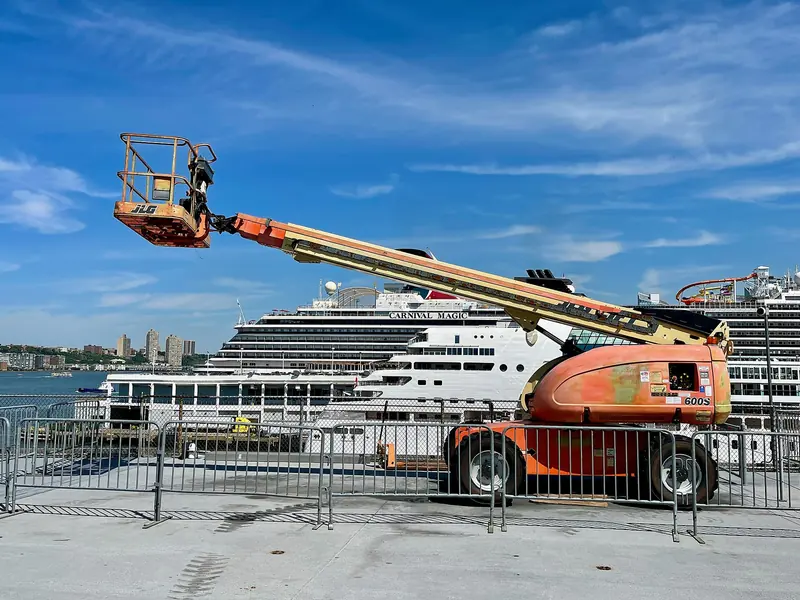 An orange JLG 600S telescopic boom lift with its boom extended, behind safety barriers.