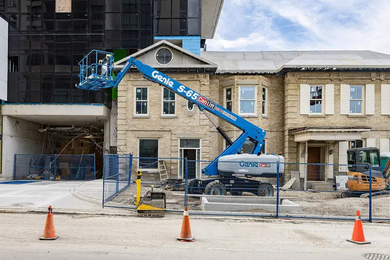 A blue Genie S-65 boom lift with its basket raised beside a building under construction, with traffic cones and fencing in front.