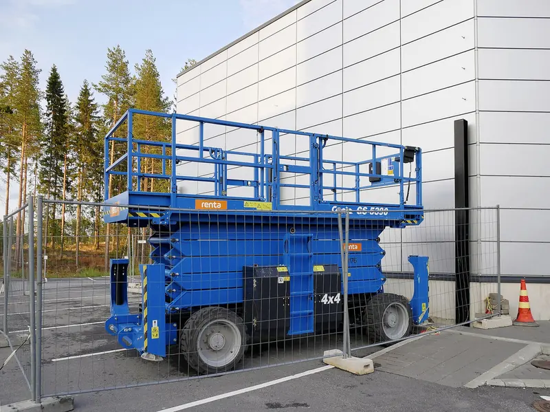 A blue Genie GS-5390 rough-terrain scissor lift with its platform lowered, parked beside a large industrial building.